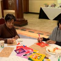 Two women decorating lunch bags for Kids' Food Basket